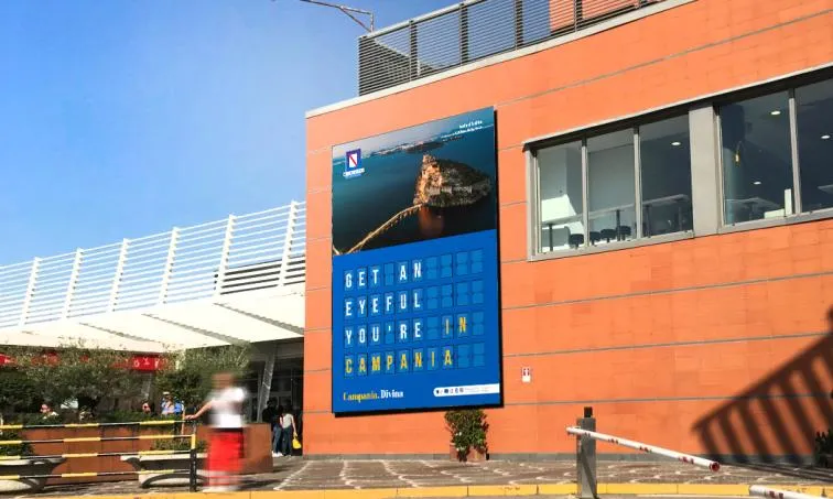 Affissione in stile tabellone partenze «Get an eyeful, you’re in Campania» sulla facciata dell’Aeroporto di Napoli