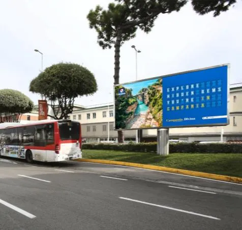 Billboard Campania.Divina all’esterno dell’aeroporto con un autobus in transito