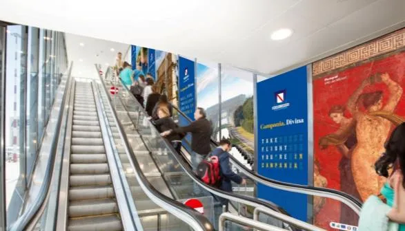 Sequenza di pannelli Campania.Divina lungo le scale mobili dell’aeroporto